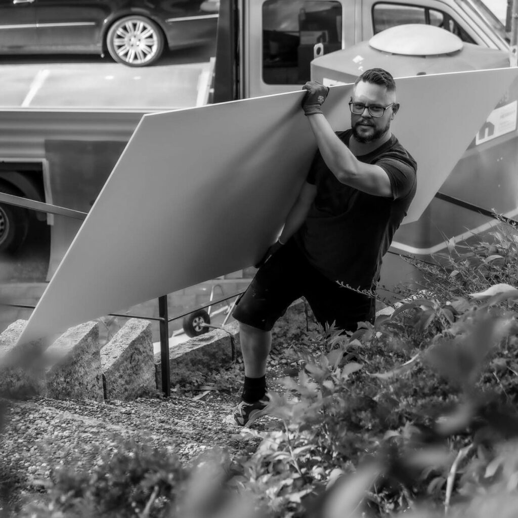 Ein Mann mit Brille und Bart trägt eine große Platte eine Treppe hinauf.