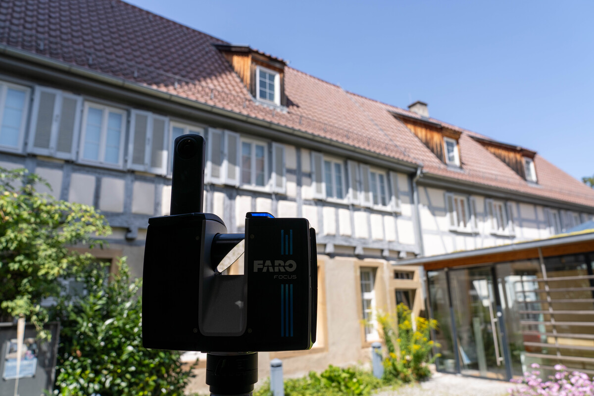 Ein schwarzes Gerät steht im Fokus vor einem alten Fachwerkhaus.